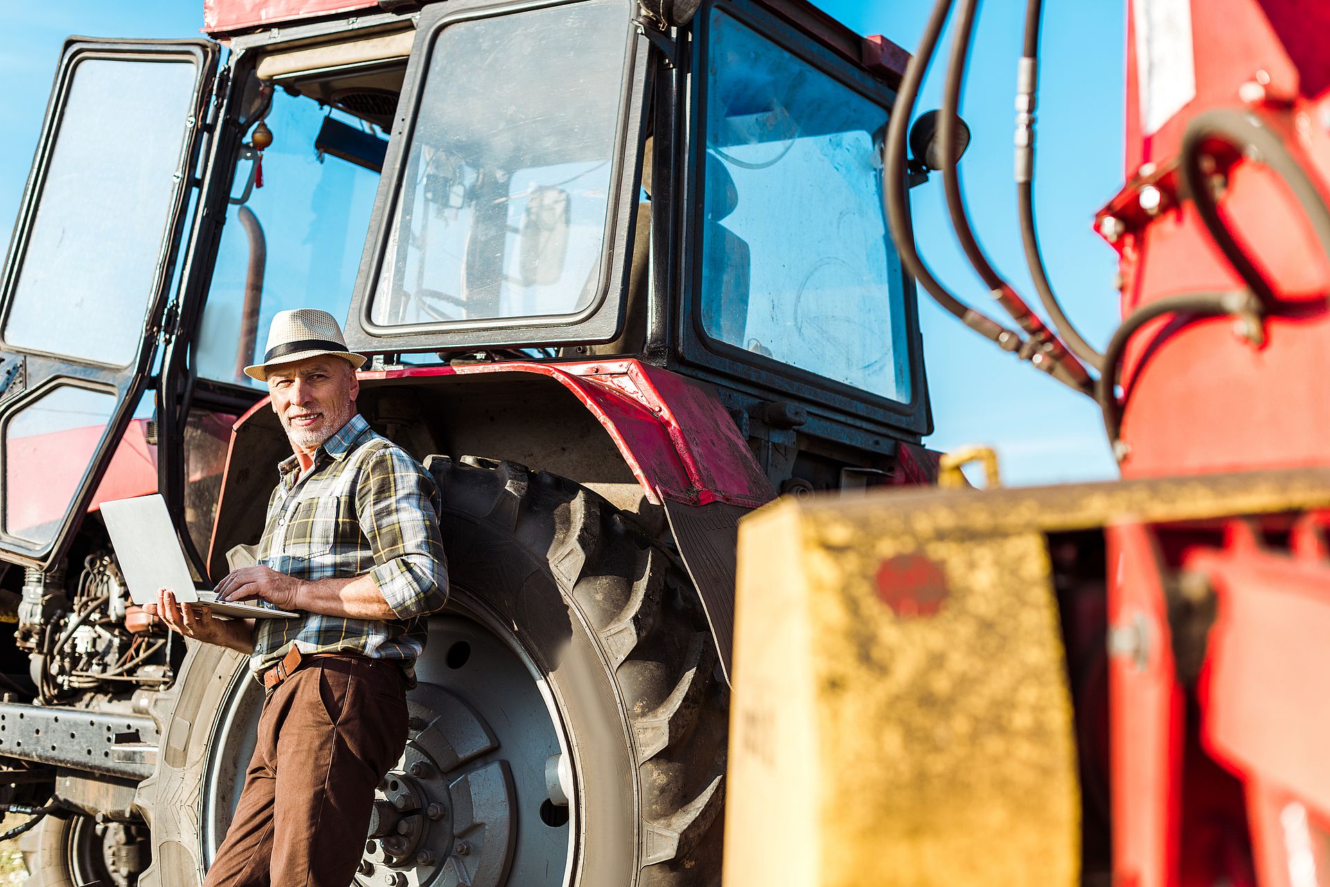 selective focus of happy farmer in straw hat using laptop near tractor